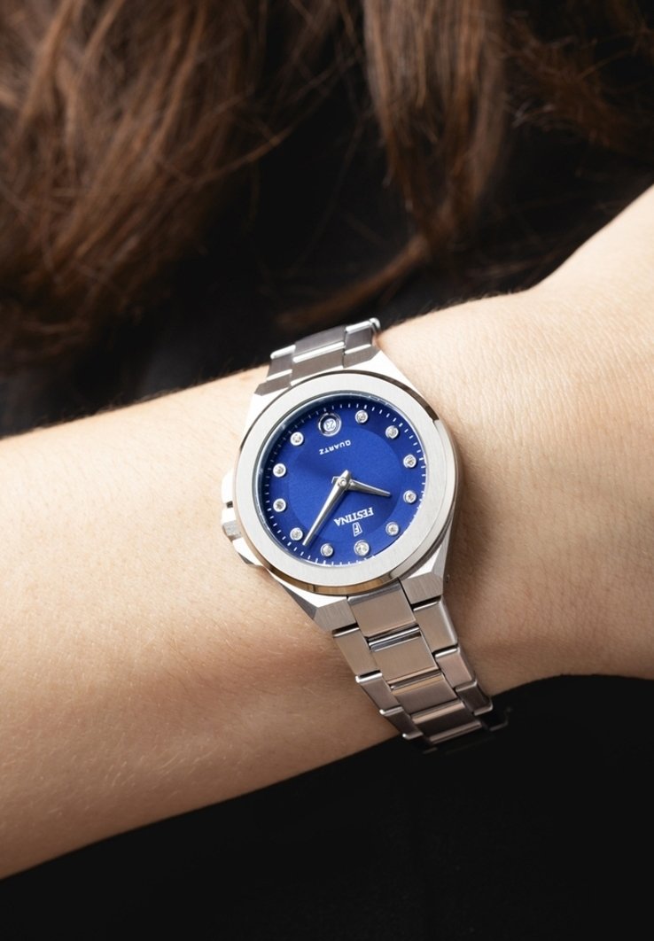 Quartsarmbandsur med blå urtavla som har diamantliknande timmarkörer, silverfärgad rostfri stålkapsel och metallarmband.