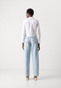 Camicia bianca con bottoni e maniche lunghe, abbinata a jeans a gamba larga di colore azzurro chiaro. L'outfit presenta una texture liscia e un design classico.