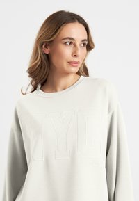Lichtgrijze sweatshirt met "NYC" borduursel, wijde ronde hals, en een ontspannen pasvorm met een zachte textuur en lange mouwen.