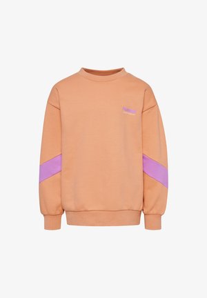 Enfant portant un sweat-shirt pêche et un short, des chaussettes blanches avec des rayures orange, et des baskets roses avec un motif chevron rouge, debout sur un fond uni.