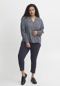 Modrá kvetinová blúzka s dlhým rukávom a výstrihom do V, voľný strih a nariasené manžety, skombinovaná s námorníckymi skrátenými nohavicami a čiernymi šľapkami.