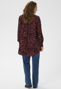 Long-sleeve, loose-fitting shirt in a red and black zebra print, paired with blue straight-leg jeans and black shoes.