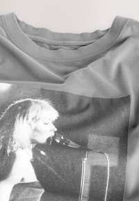 T-shirt gris avec une impression graphique en noir et blanc d'une femme chantant dans un microphone, centrée à l'avant.