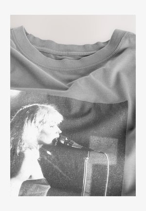 Siva majica s crno-bijelim grafičkim otiskom žene koja pjeva u mikrofon, smještenim na sredini sprijeda.