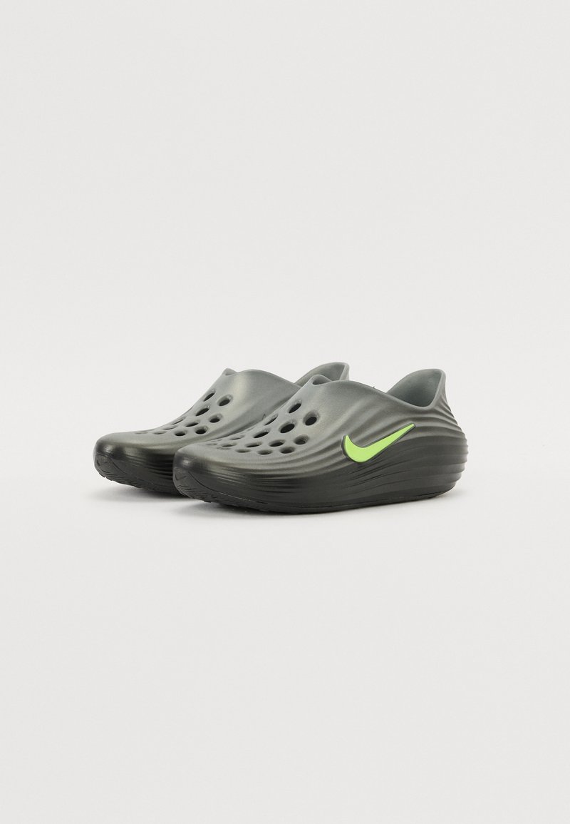Des sabots synthétiques gris présentent un design ondulé, de nombreux trous de ventilation et un accent de swoosh Nike vert vif sur le côté.