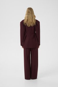 Burgundy tailored suit featuring a structured blazer with broad shoulders and wide-leg trousers, made from a smooth fabric with minimal embellishments.
