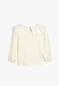 Kermansävyinen pitkähiha blusa, jossa on kerrosmainen kaulus pitsireunalla, avainaukkotakakiinnitys ja gatheroitut hihat.