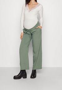 Gröna vida byxor av mjukt tyg med elastisk midja och sidofickor. Matchade med en vit ribbad långärmad topp med spetsdetaljer.