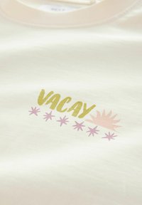 Bijela pamučna dukserica s natpisom "VACAY" u zelenoj i ružičastoj boji, okružena motivima zvijezda svijetlo ružičaste boje, smještena u središtu prednje strane.