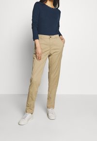 Maglietta a maniche lunghe blu navy con borchie decorative sul colletto, abbinata a pantaloni chinos beige chiaro e sneakers bianche. Design semplice e vestibilità slim.