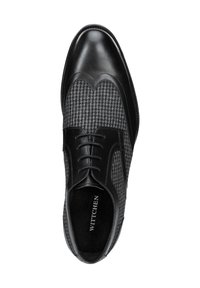 Zapato de cuero negro con tejido a rayas houndstooth, punta afilada, diseño con cordones y planta interior negra texturizada. Logotipo de la marca visible en el interior.
