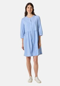Abito a righe azzurro chiaro con scollatura arrotondata, maniche a tre quarti, bottone frontale e vita arricciata, abbinato a sneakers bianche.