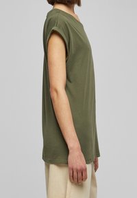 Olivově zelené triko s krátkým rukávem a volným střihem, s ohrnutými manžetami, vyrobené z měkké bavlny. Jednoduchý, čistý design s kulatým výstřihem.