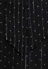 Tessuto nero con strisce verticali argento e pois bianchi. La texture appare leggera e ariosa, con una finitura liscia.