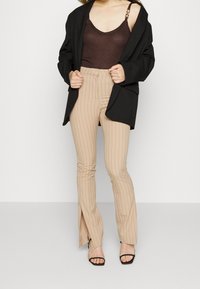 Beige stribede flared bukser med sideslids, parret med en mørkebrun tanktop og en løs sort blazer.