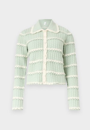 Ανοιχτό πράσινο πλεκτό ζακέτα με κρεμ οριζόντιες λωρίδες με κυματιστό σχέδιο, κούμπωμα με κουμπιά μπροστά και μυτερό γιακά πάνω σε απλό φόντο.