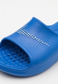 Blue rubber slide sandal featuring a textured footbed, open toe design, and white studded accents on the upper for decoration.