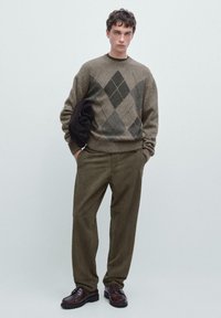 Olivengrøn argyle sweater med grå mønstre, parret med olivenfarvede kordfløjlshbukser. Brune lædersko og en mørk taske fuldender looket.