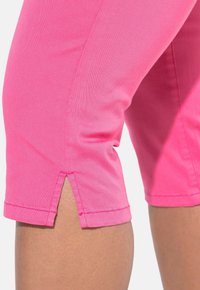 Vaaleanpunaiset polvipituiset shortsit, jotka on valmistettu pehmeästä kankaasta, ja niissä on sivuhalkiot helmassa. Ne ovat sileäpintaiset ja suoran leikkuun omaavat.