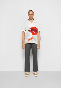 Chemise blanche à manches courtes avec un motif de lèvres rouges, associée à un pantalon gris foncé et des baskets beiges. Design minimal, coupe décontractée.