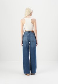 Jeans din denim albastru, cu talie înaltă și picioare largi, cu un finisaj curat, având buzunare la spate și o etichetă din piele maro la talie.
