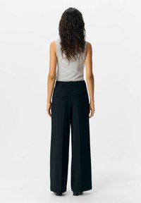 Schwarze, weit geschnittene Hose mit Gesäßtaschen, kombiniert mit einem grauen, ärmellosen Oberteil. Verfügt über eine glatte Textur und eine klare Silhouette.