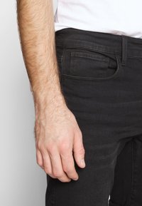 Pánské černé džíny se slim fit; vyrobené z denimu; mají klasický pětikusový design a viditelné švy na kapsách.