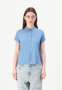 Light blue short-sleeve button-up shirt made from a smooth fabric with a collared neck and rolled sleeves, paired with loose denim pants.