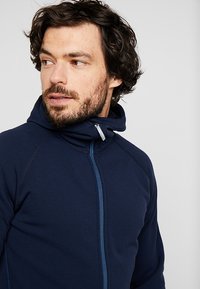 Mornarica flis jakna s visokim ovratnikom, punim zatvaračem i plavim akcentnim šavom. Ima mekanu teksturu i rukave raglan za udobnost.