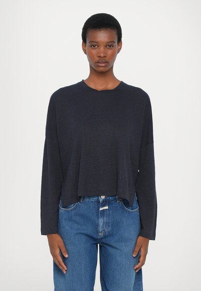 Marineblauw longsleeve shirt met een ontspannen pasvorm en ronde hals, gecombineerd met high-waisted denim jeans. Soepele textuur en minimalistisch ontwerp.