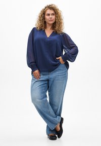 Blouse en satin bleu marine, avec un décolleté en V et des manches bouffantes. Associée à un jean bleu clair, coupe décontractée, et des sandales noires.