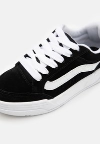 Schwarze Wildledersneaker mit weißen Schnürsenkeln, ausgestattet mit einem markanten weißen Seitenstreifen und einer strukturierten Sohle, die ein klassisches sportliches Design hervorhebt.