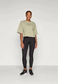 Olive green cropped t-shirt with short sleeves and a circular print on the chest, paired with tight black leggings and black sneakers.