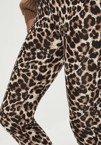 Leopardmönstrade leggings med en blandning av svarta och bruna fläckar på en ljusbeige bakgrund, tillverkade av ett mjukt och stretchy material.