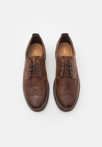 Zapatos de cuero marrón con cordones y detalles de brogue, que presentan un acabado suave, puntera redonda y suela de goma de contraste.