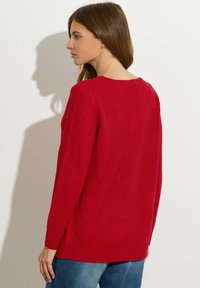 Czerwony sweter z prążkowanego materiału, z okrągłym dekoltem, bocznymi rozporkami i długimi rękawami. Uzupełniony gładką fakturą i luźnym krojem.