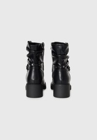 Paire de bottes en cuir noir mi-mollet avec talons blocs, fermetures éclair et lanières décoratives avec clous en métal à l'arrière.