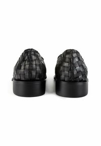 Zwarte geweven lederen schoenen met een lage, ronde zwarte zool, met een gestructureerd oppervlak en fijne stikdetails aan de achterkant.
