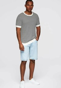 Camisa de punto rayada en blanco y negro con mangas cortas, combinada con pantalones cortos de mezclilla azul claro. Zapatillas blancas completan el conjunto.