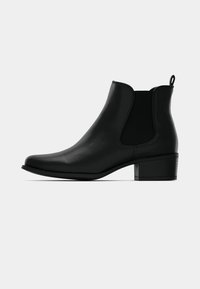 Botín de cuero negro con punta redonda, paneles laterales elásticos y un tacón corto apilado. Cuenta con una pequeña lengüeta en la parte trasera.