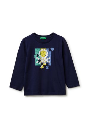 Camiseta de manga larga azul marino con un gráfico de rompecabezas colorido que muestra una forma de círculo y cruz, con varias piezas del rompecabezas faltantes o flotando.