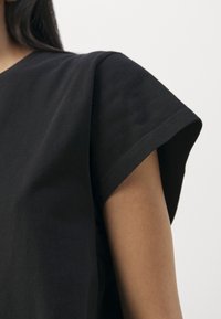 T-shirt en coton noir avec manches courtes retroussées et coupe décontractée. Couture de col visible et texture douce et lisse.