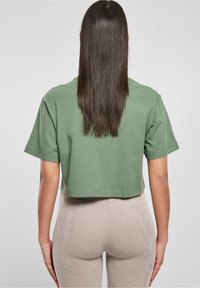 Zelené zkrácené tričko s krátkými rukávy, hladkou strukturou a kulatým výstřihem, spojené se světlými béžovými ribbed kalhotami.