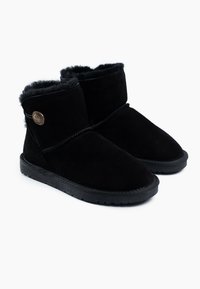 Botines de ante negro con suave forro de piel sintética, que presentan un acento de logo metálico redondo y una suela de goma texturizada.