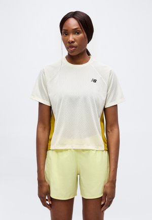 Femme portant un t-shirt de sport en mesh jaune clair avec des panneaux latéraux moutarde et un short jaune clair, debout devant un fond uni.