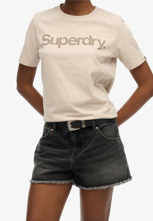 Beżowa koszulka z krótkim rękawem z logo "Superdry" w połączeniu z czarnymi szortami jeansowymi z postrzępionym wykończeniem i czarnym paskiem ze srebrną klamrą.