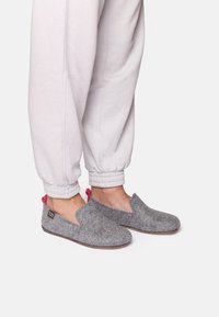 Gray felt slip-on shoes with a round toe and pink accents, paired with light gray jogger pants with elastic cuffs.