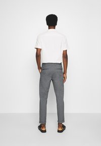 Biała koszula z krótkim rękawem, dopasowane szare spodnie. Spodnie mają gładką fakturę i podwinięte mankiety. Wygląd dopełniają sandały.