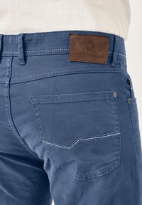 Blue cotton pants with a smooth texture, featuring a brown leather tag with "redpoint" embossed, and contrasting stitching on the back pockets.