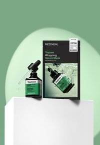 Flacon de sérum Mediheal Teatree Calming Hydra avec compte-gouttes et emballage du masque sérum Teatree Wrapping sur fond vert et blanc.